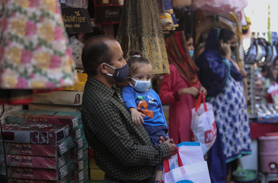 A man carries a child, both wearing masks as a precaution against the coronavirus as he shops at a market ahead of Hindu festivals in Jammu, India, Thursday, Oct.29, 2020. India's confirmed coronavirus caseload surpassed 8 million on Thursday with daily infections dipping to the lowest level this week, as concerns grew over a major Hindu festival season and winter setting in. (AP Photo/Channi Anand)