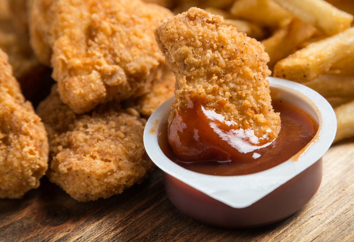 Chicken nuggets dipping in a BBQ sauce container and french fries