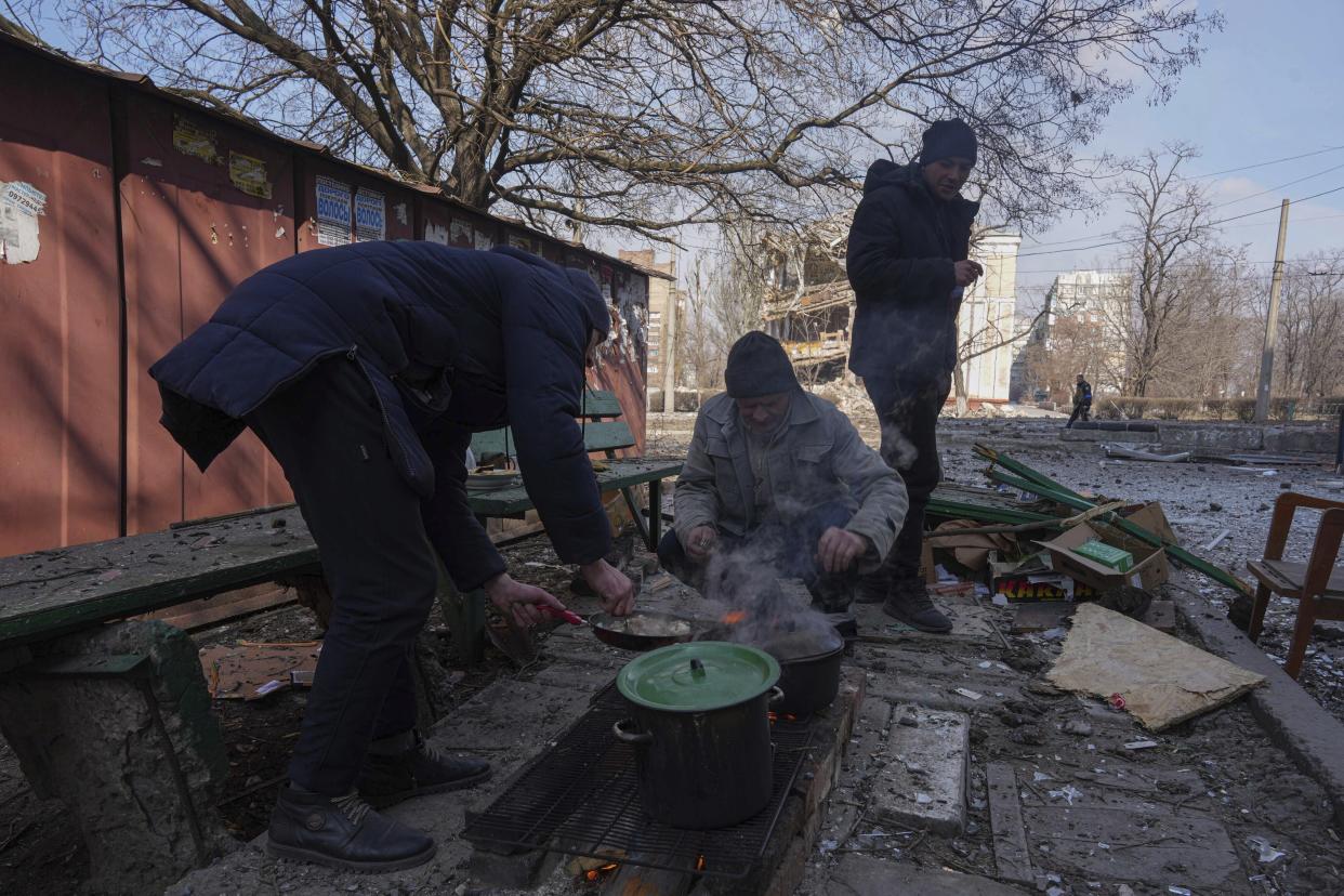 Men cook a meal in a street in Mariupol, Ukraine, Sunday, March 13, 2022. The surrounded southern city of Mariupol, where the war has produced some of the greatest human suffering, remained cut off despite earlier talks on creating aid or evacuation convoys. (AP Photo/Evgeniy Maloletka)