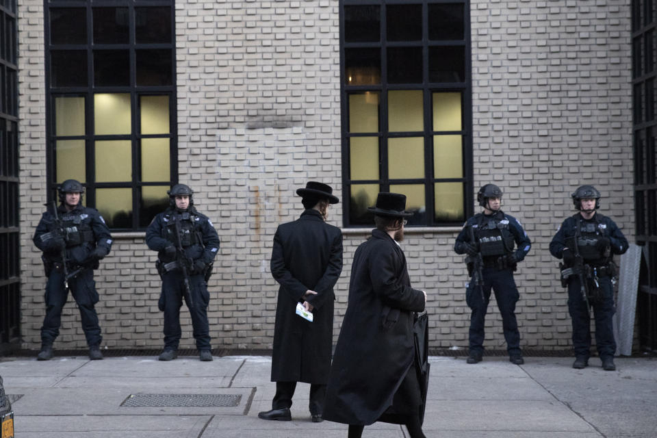 Orthodox Jewish men pass New York City police guarding a Brooklyn synagogue prior to a funeral for Mosche Deutsch, Wednesday, Dec. 11, 2019 in New York. Deutsch, a rabbinical student from Brooklyn, was killed Tuesday in the shooting inside a Jersey City, N.J. market. (AP Photo/Mark Lennihan)