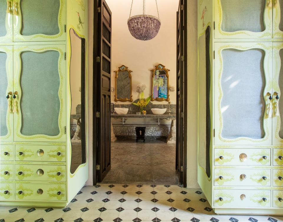 A pair of hand-painted custom armoires flank the hallway leading from the primary bedroom into the bath. In the bath, Skouras designed the amethyst–and–rock crystal light fixture, the vanity, and the lapis lazuli hand-painted mirrors.