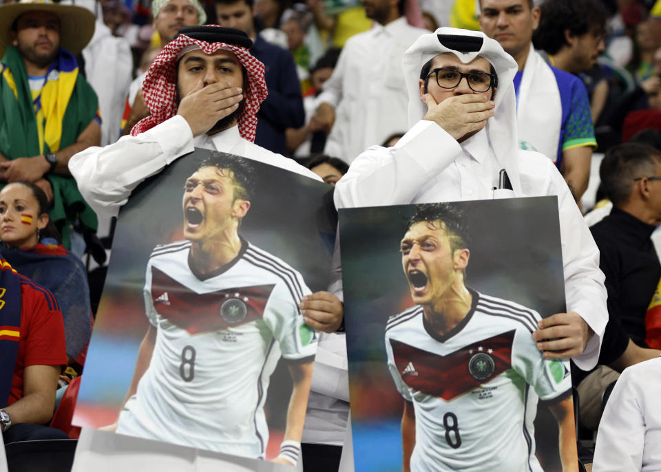 Soccer Football - FIFA World Cup Qatar 2022 - Group E - Spain v Germany - Al Bayt Stadium, Al Khor, Qatar - November 27, 2022 Fans cover their mouths while holding pictures of former Germany player Mesut Ozil REUTERS/John Sibley