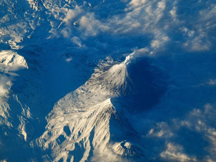 volcano emits vapor above snowy mountains