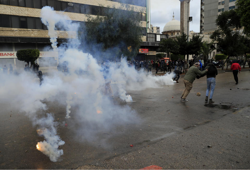 Protesters run from tear gas canisters during a protest against deteriorating living conditions and strict coronavirus lockdown measures, in Tripoli, north Lebanon, Thursday, Jan. 28, 2021. Violent confrontations between protesters and security forces over the last three days in northern Lebanon left a 30-year-old man dead and more than 220 people injured, the state news agency said Thursday. (AP Photo/Hussein Malla)