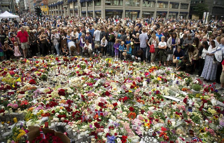 People crowd in Oslo around a flower tribute to the victims of a bomb explosion which ripped through government buildings and the shooting spree at a youth camp two days ago. Suspected Norwegian mass killer Anders Behring Breivik faces justice Monday, after Oslo police defended the hour it took to reach the island where most of his 93 victims died in a hail of bullets