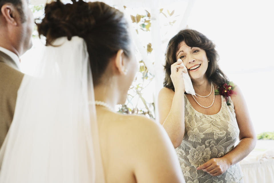 Woman in a patterned dress wipes a tear during a wedding while bride looks on