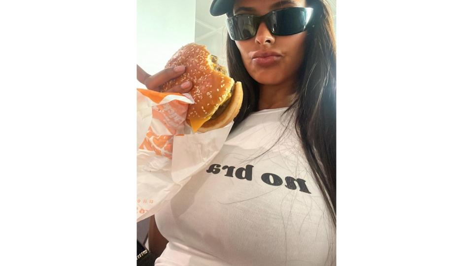 Maya Jama eats a cheeseburger in a graphic tee