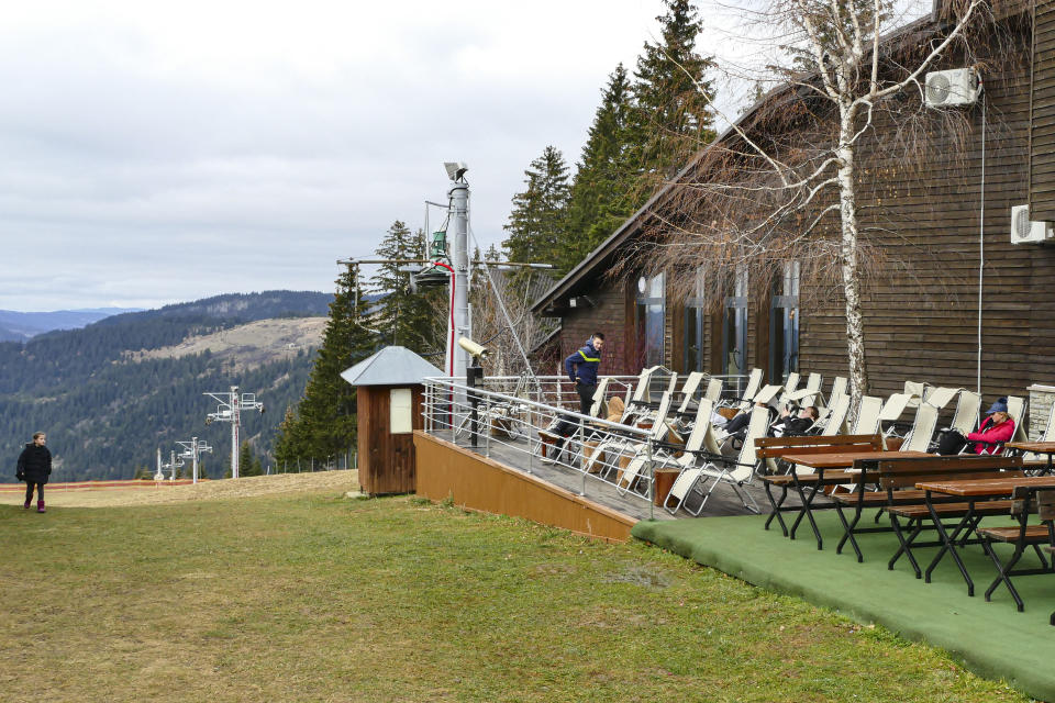 Tourists sit on the terrace of a hotel in Vlasic, a ski resort affected by unusual warm weather in Bosnia, Tuesday, Jan. 3, 2023. The exceptional wintertime warmth is affecting ski resorts across Bosnia, prompting tourism authorities in parts of the country to consider declaring a state of natural emergency. (AP Photo/Almir Alic)