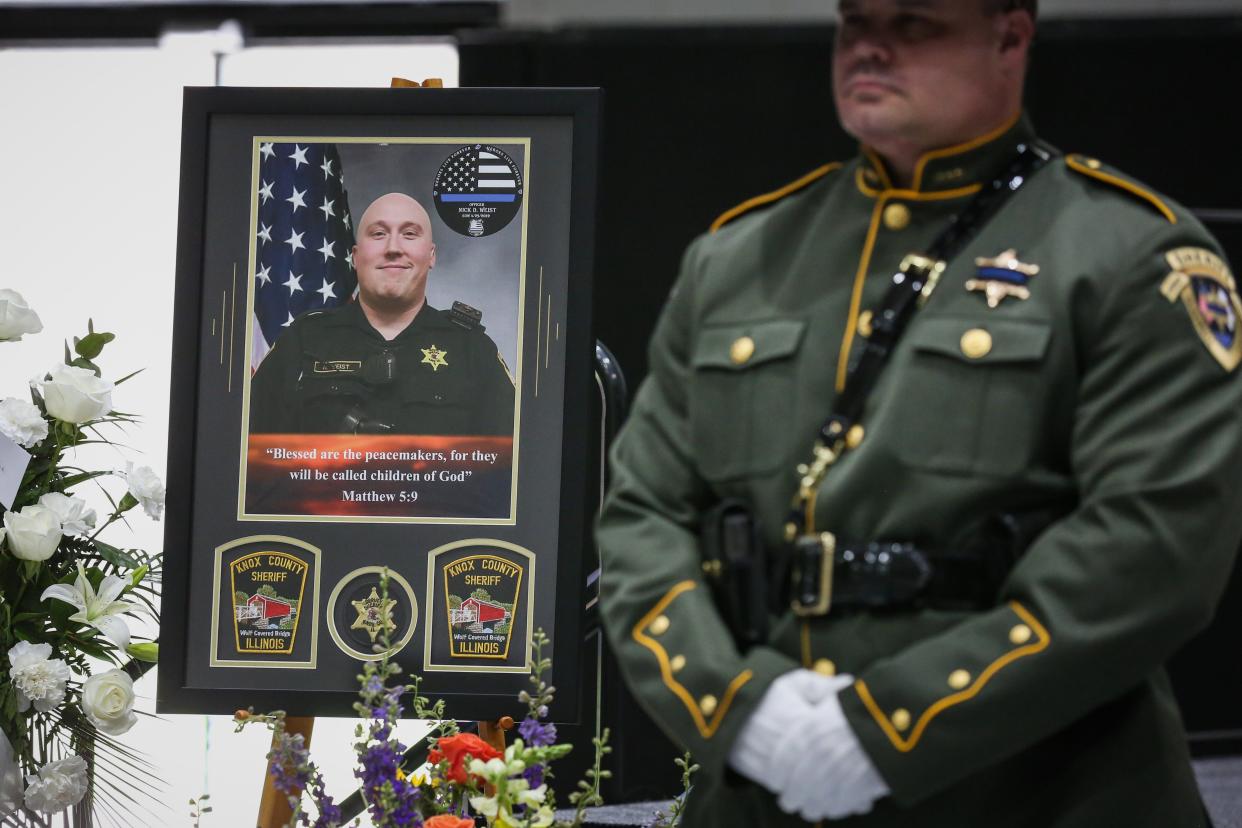 A frame containing a photo, badge and patches of fallen Knox County Sheriff's Deputy Nicholas Weist stands near the casket during a memorial service at Galesburg High School on Saturday, May 7, 2022. Weist was hit and killed by a car April 29 as he was setting out spike strips at the intersection of U.S. Route 150 and 150th Avenue near Alpha to stop a vehicle fleeing from Galesburg police.