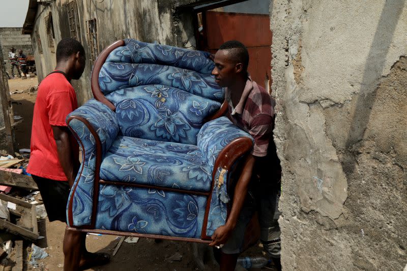 Men carry an armchair as they prepare to leave their house at Adjoufou in the area around Felix Houphouet Boigny airport in Abidjan