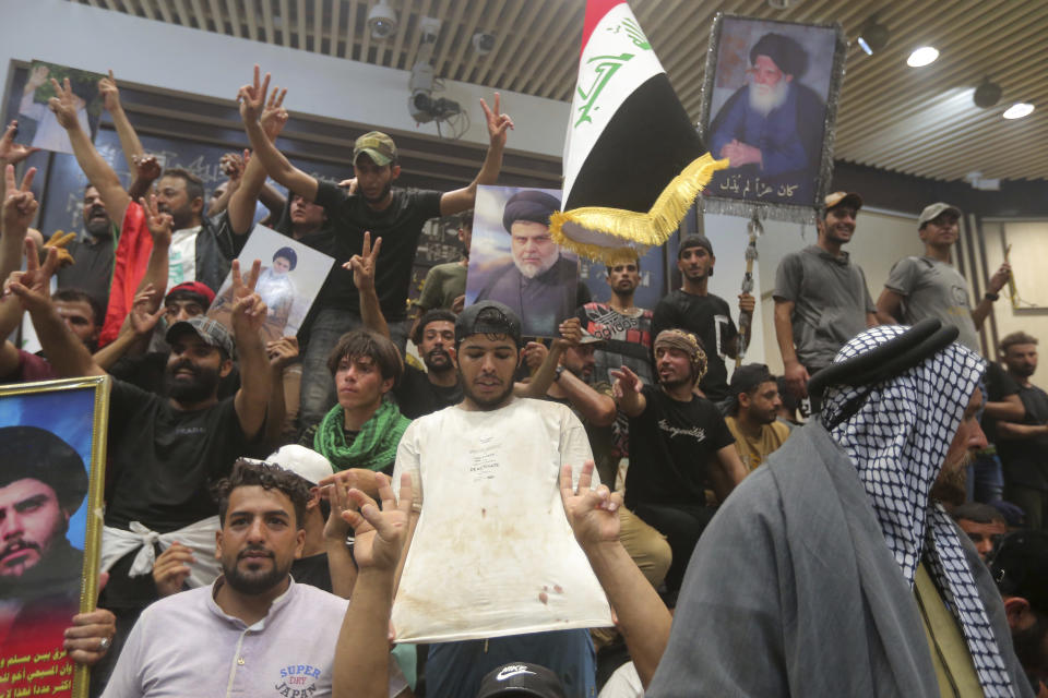 Iraqi protesters pose with national flags, a blood-stained shirt, and pictures of Shiite cleric Muqtada al-Sadr inside the Parliament building in Baghdad, Iraq, Saturday, July 30, 2022. Thousands of followers of the influential Shiite cleric breached Iraq's parliament on Saturday, the second time in a week, to protest the government formation efforts lead by Iran-backed groups.(AP Photo/Anmar Khalil)