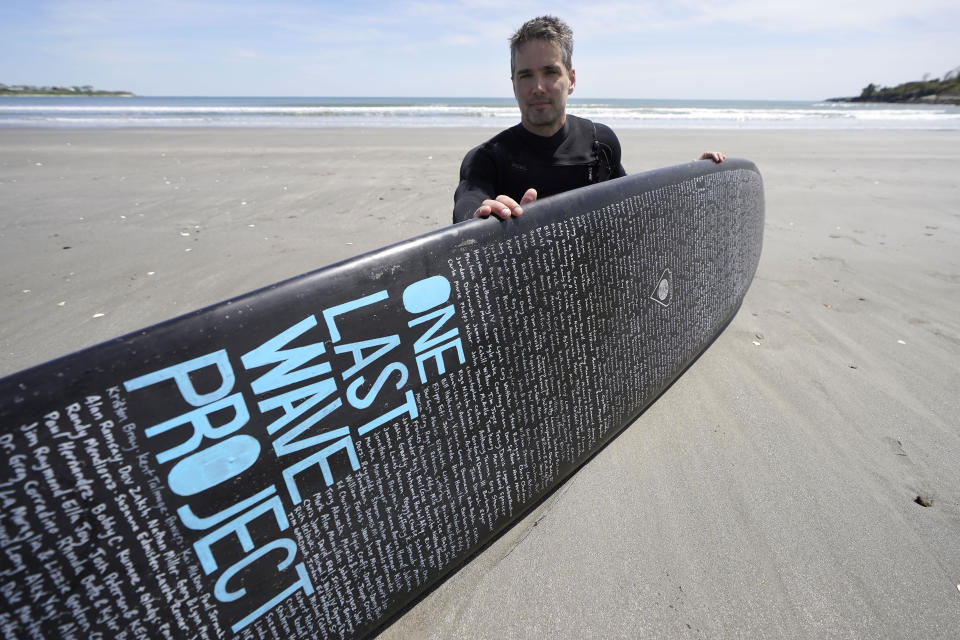 Dan Fischer, of Newport, R.I., sits for a photograph with his surfboard on Easton's Beach, in Newport, Wednesday, May 18, 2022. Fischer, 42, created the One Last Wave Project in January 2022 to use the healing power of the ocean to help families coping with a loss, as it helped him following the death of his father. Fischer places names onto his surfboards, then takes the surfboards out into the ocean as a way to memorialize the lost loved ones in a place that was meaningful to them. (AP Photo/Steven Senne)