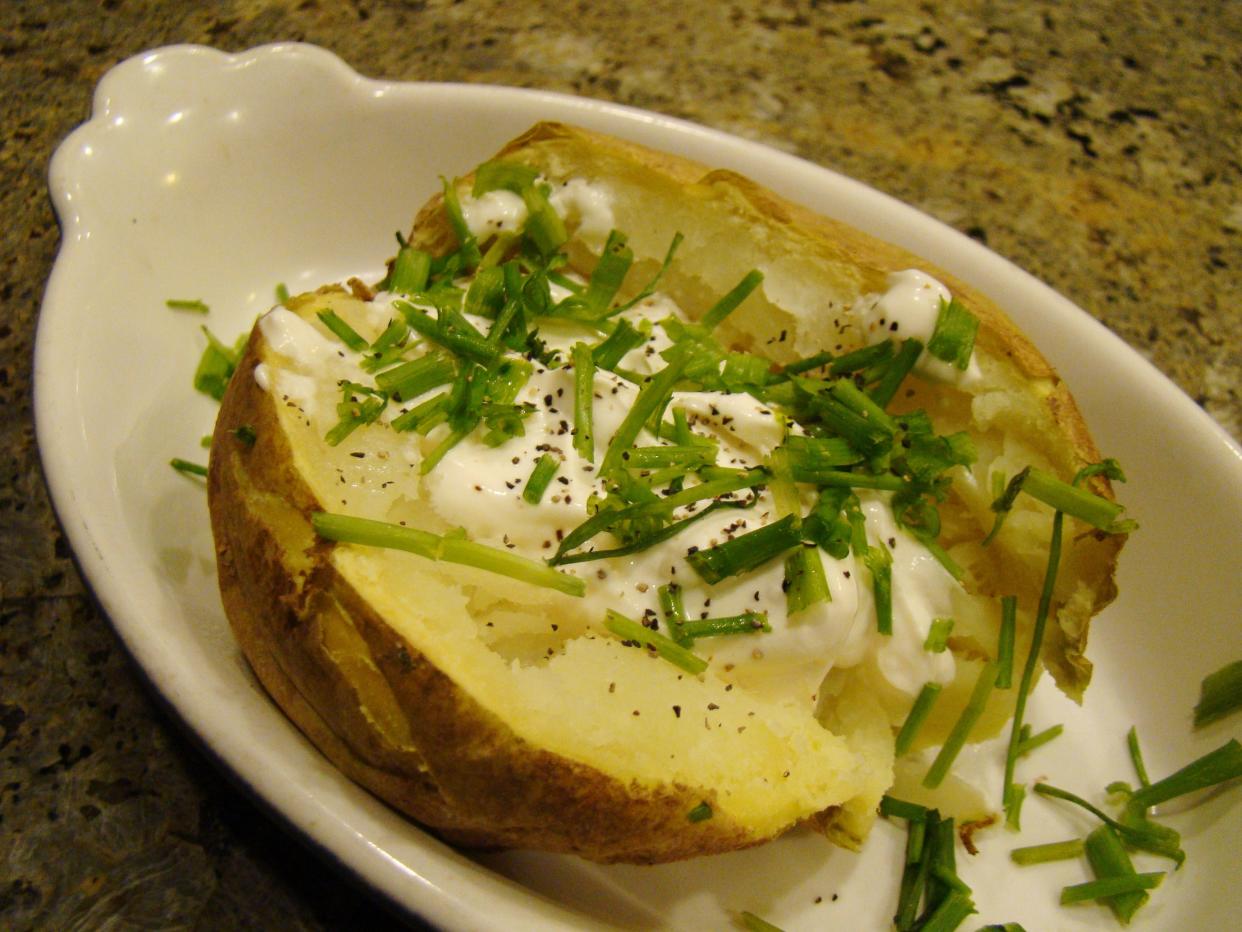 Baked potato with chives, black pepper and sour cream on a white plate.