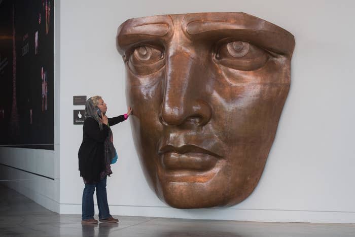 Woman touches a large bronze face sculpture on a wall, appearing reflective and contemplative