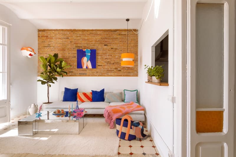 Living room with brick wall, framed artwork, and white couch with decorative pillows.