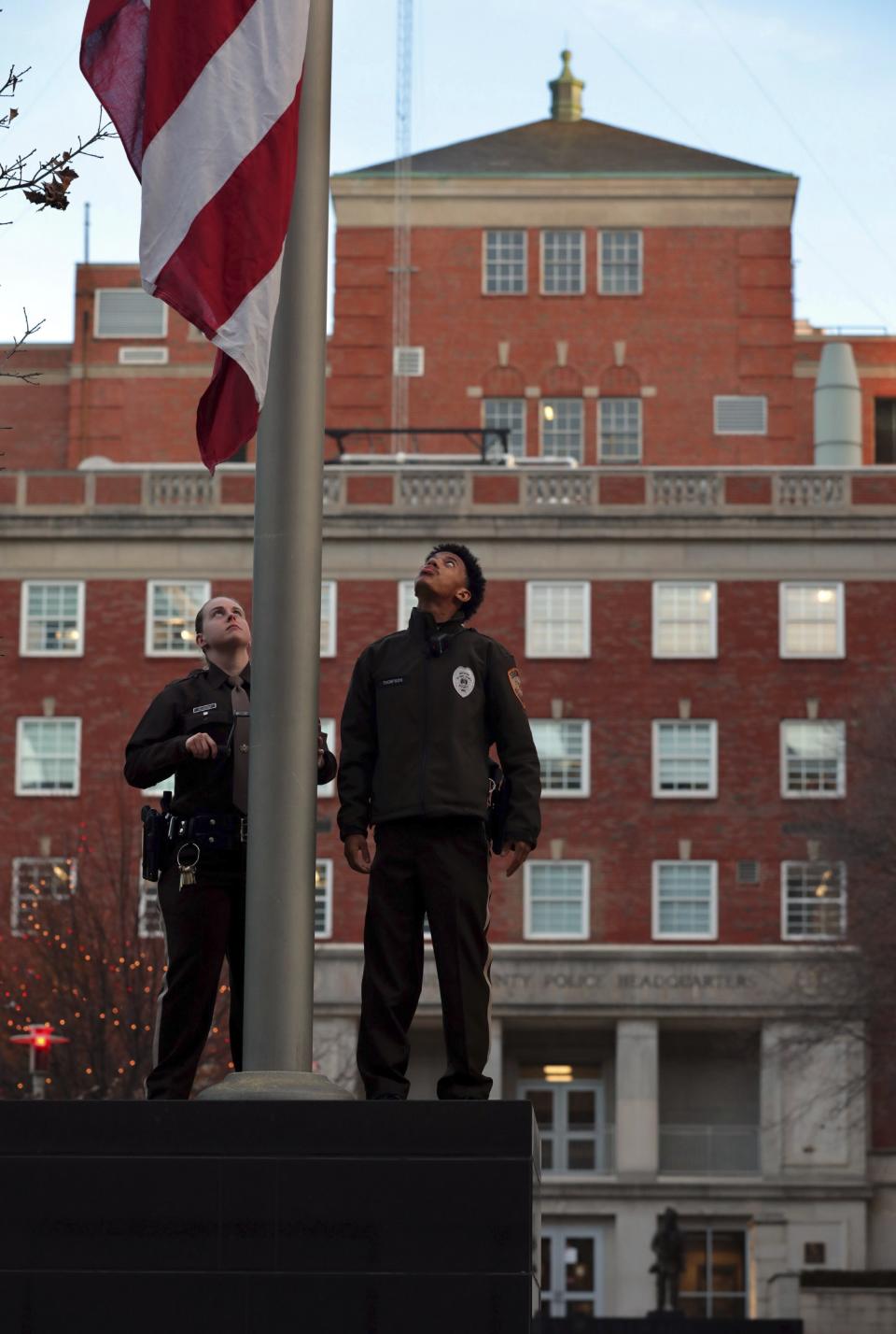 St. Louis County police security officers Brittany Billington and Marshall Thompson lower a flag outside county police headquarters in Clayton, Mo., on Thursday, Dec. 2, 2021, in memory of county police officer Antonio Valentine. The St. Louis County police detective died in the line of duty and a suspect he was trying to stop also died in a head-on collision of their vehicles. The crash happened Wednesday, Dec. 1, 2021, in north St. Louis County after officers with the department’s drug unit tried to stop a car that had been reported stolen, police said. (Robert Cohen/St. Louis Post-Dispatch via AP)