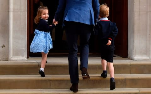 Princess Charlotte of Cambridge (left) turns to wave at the media as she is led in with her brother Prince George of Cambridge (right) - Credit: Ben Stansall/AFP