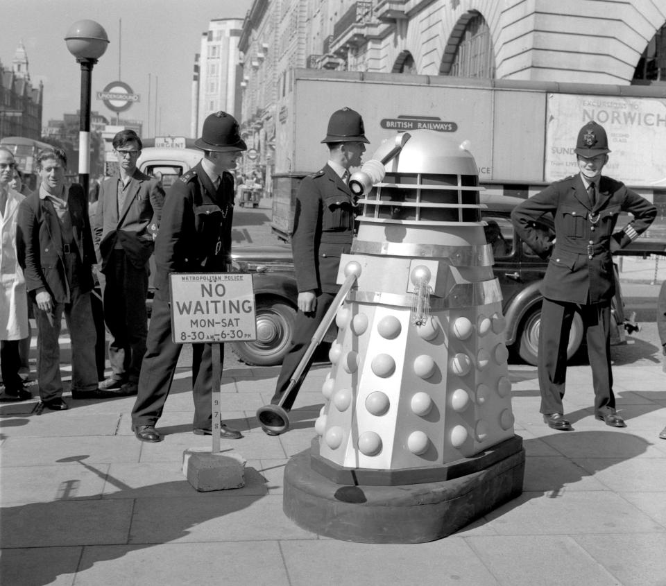 Policemen waiting for a Dalek, parked alongside a "no waiting" sign, to be moved by BBC technicians. The Daleks were in London for location shooting of a new "Dr Who" series.