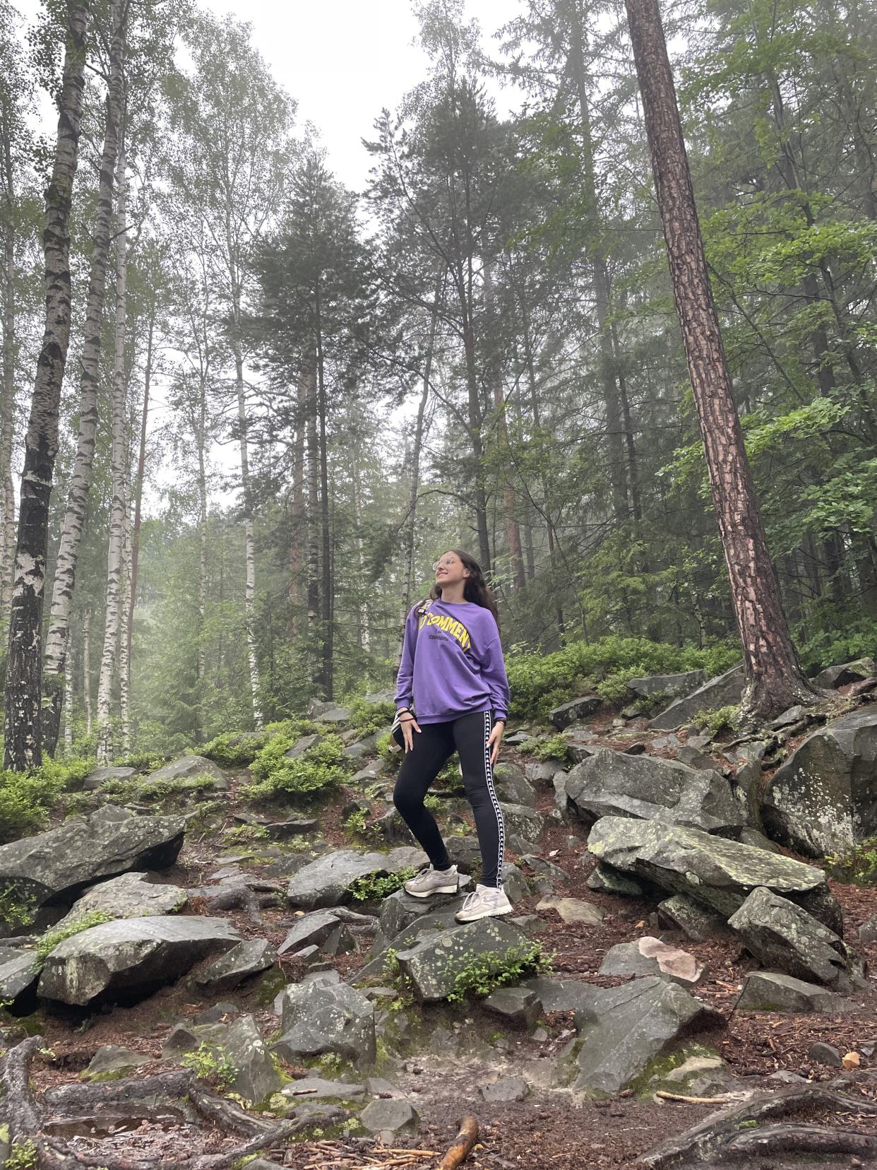 A photo of Solomiya standing on top of a rock in a forest 