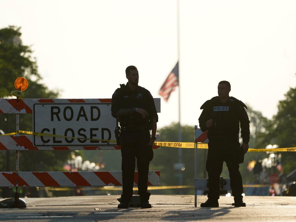 Two police officers stand their post, the day after a deadly mass shooting, on the Westside of the Highland Park, Ill., Tuesday, July 5, 2022.