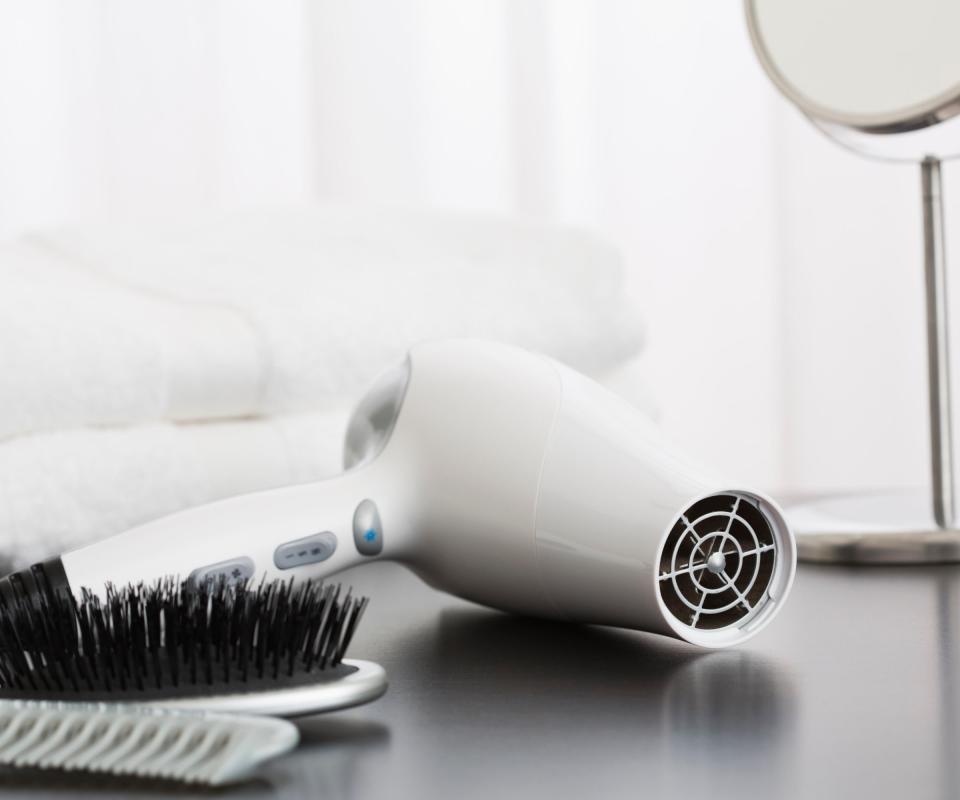 A white hairdryer laying on a table beside a black brush