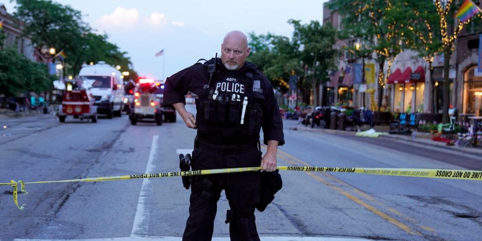 A police officer holds up police tape at the scene of a mass shooting at the Fourth of July parade in downtown Highland Park, a Chicago suburb, on Monday, July 4, 2022.