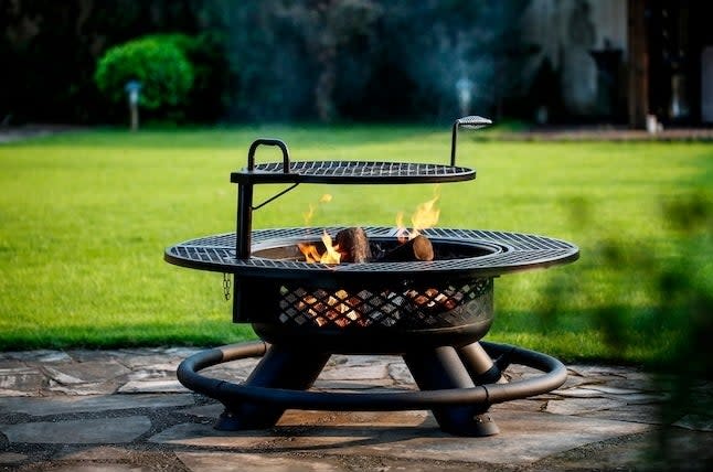 A wood burning fire pit with grill outside in a yard