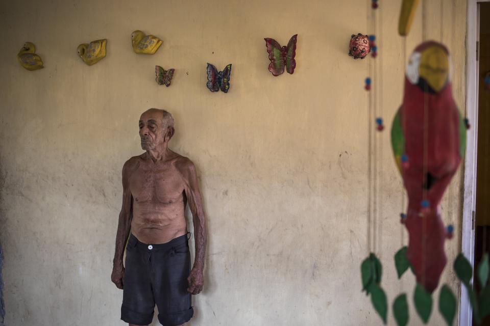 Jose Calderon, 86, stands next to wall adornments given to him by neighbors in "Los Hijos de Dios" neighborhood in Maracaibo, Venezuela, Wednesday, Nov. 20, 2019. Few in Maracaibo have responded to Venezuelan opposition leader Juan Guaido's efforts to reignite his movement, despite it being a city hard hit by crisis. Its residents endure daily power outages in a region that’s punishingly hot. (AP Photo/Rodrigo Abd)