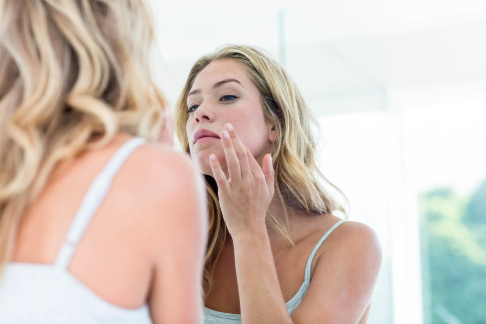 Focused beautiful young woman looking at herself in the bathroom mirror at home