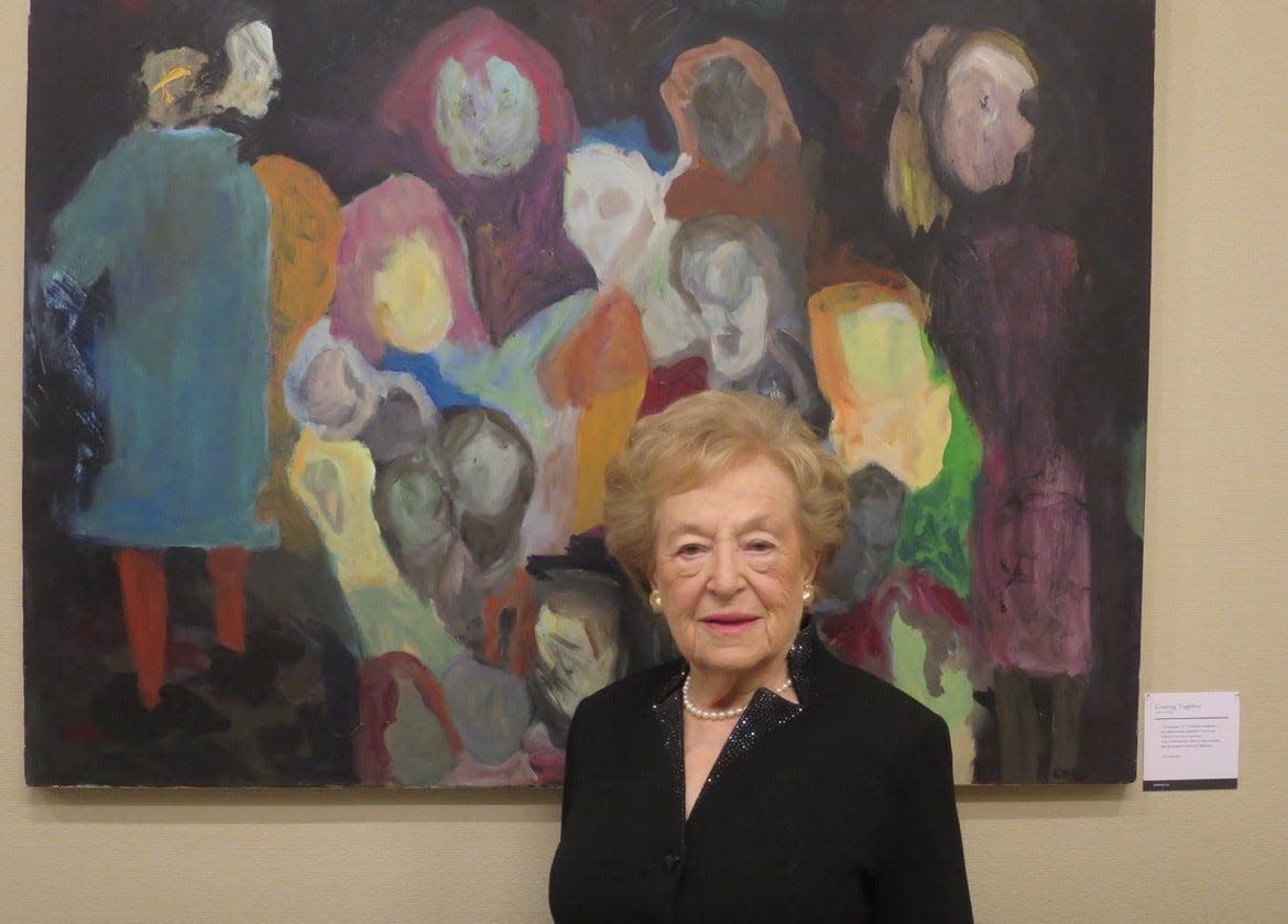 Ruth Oppenheim's experience escaping Nazi Germany and surviving the Holocaust is the inspiration behind an art exhibit by her daughter, Claudia Cameron, which will be open for the public to view on Dec. 19 in Falmouth. Pictured is Ruth Oppenheim, now 95, in front of one of her daughter's paintings at a past exhibit of the work. This is just the second time the work is being exhibited.