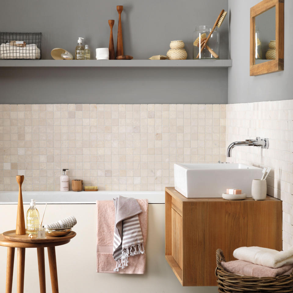 Grey Bathroom, slate flooring, modern bathroom sink, square white ceramic basin on light wood wall mounted storage unit, travertine mosaic tiled wall, built in chrome wall taps, white bath, pine side tables, wicker storage basket, high shelf containing toiletries