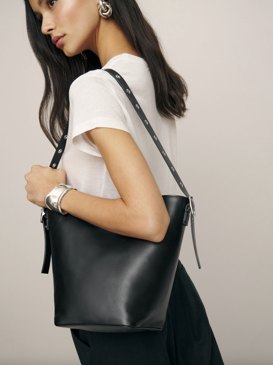 model wearing white t-shirt and black leather bag, Rafaella Medium Trapeze Tote (Photo via Reformation)