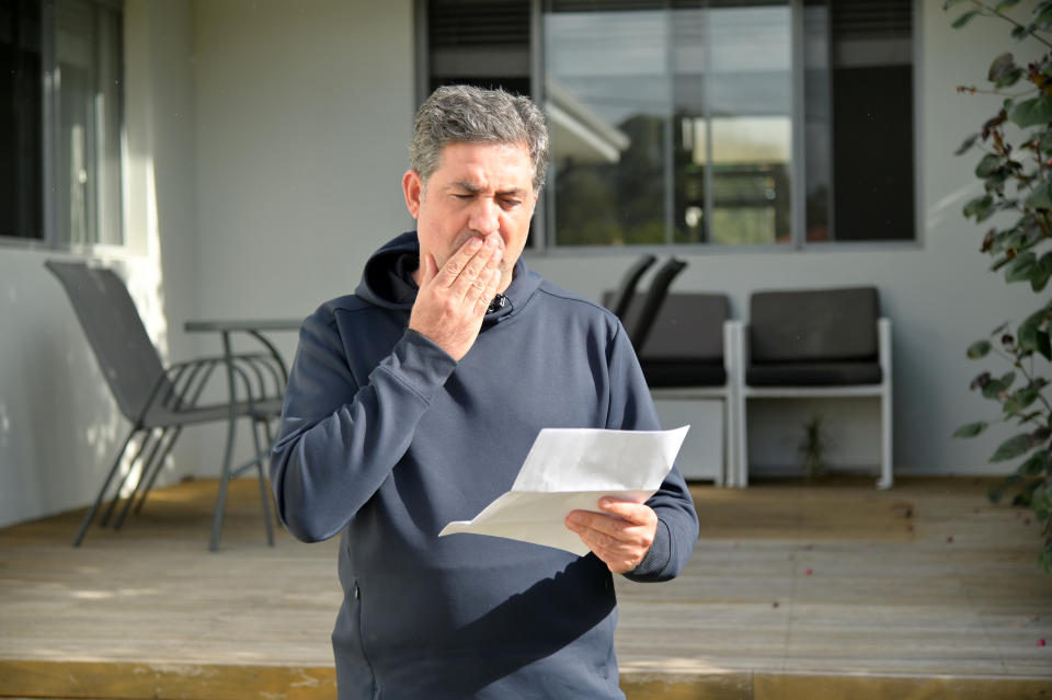 Man looks shocked while reading a letter outside a home front door.