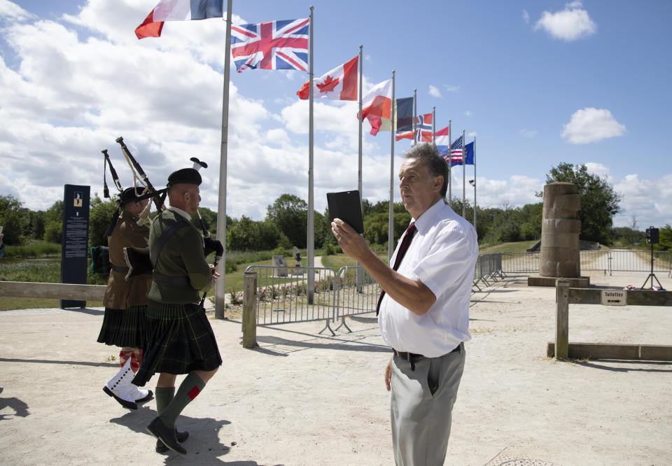 British expatriate Steven Oldrid, right, films a group crossing over the site of the original WWII Pegasus Bridge during D-Day ceremonies in Benouville, Normandy, France on Saturday, June 6, 2020. Due to coronavirus measures many relatives and veterans will not make this years 76th anniversary of D-Day. Oldrid will be bringing it to them virtually as he places wreaths and crosses for families and posts the moments on his facebook page. (AP Photo/Virginia Mayo)