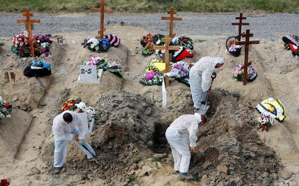 Grave diggers wearing personal protective equipment bury a person at a graveyard in Saint Petersburg - REUTERS/Anton Vaganov