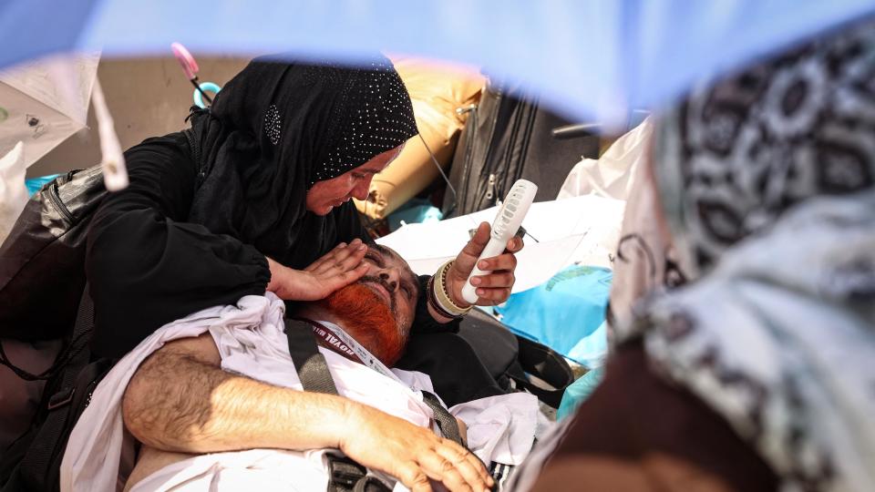 A woman uses a hand held battery run fan to cool off a man lying on the ground, affected by the scorching heat, during the symbolic 'stoning of the devil' ritual at the annual hajj pilgrimage in Mina on 16 June 2024