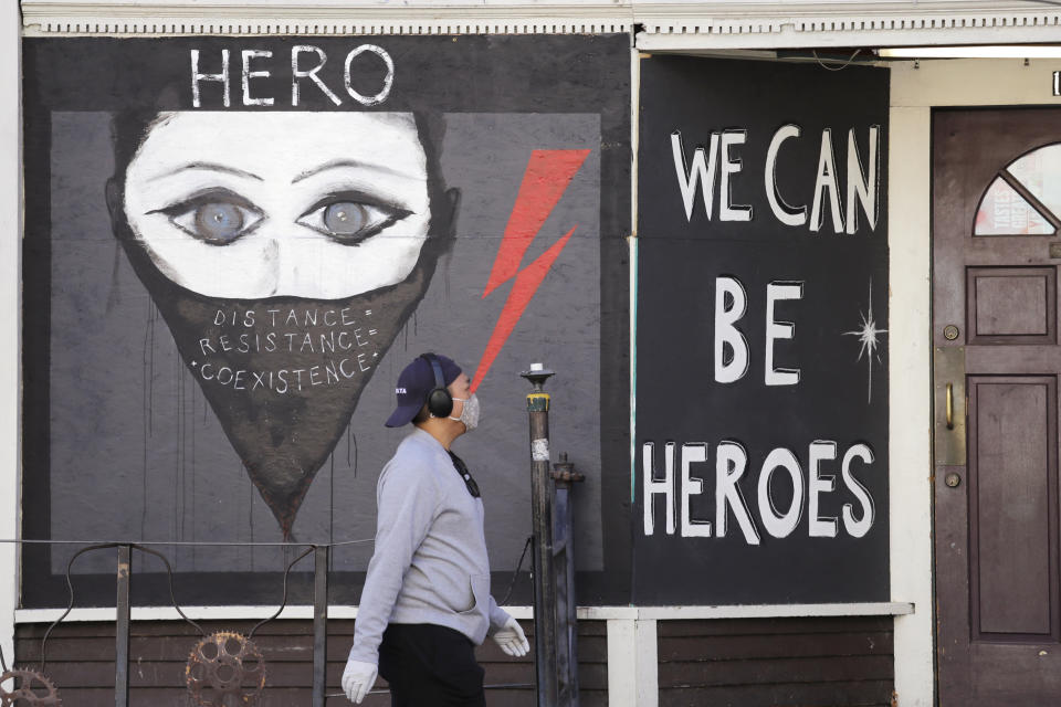 A pedestrian walks past artwork painted on plywood covering a business closed during the coronavirus outbreak Thursday, April 16, 2020, in Seattle. More than 585,000 people in Washington sought unemployment benefits last week, with 143,000 people filing claims for the first time as businesses remain closed or with limited operations due to the stay-at-home order issued due to the cororavirus pandemic, state officials said Thursday. (AP Photo/Elaine Thompson)