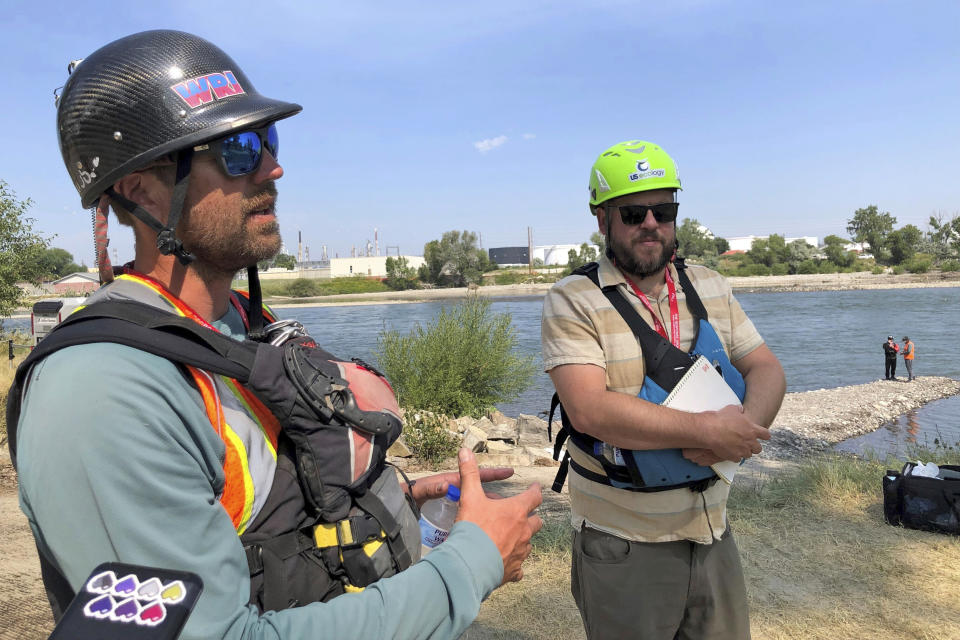 Cleanup group supervisor Cody Harris speaks about the recovery of oil product from a train accident last month as Kevin Stone with the Montana Department of Environmental Quality listens at a boat launch along the Yellowstone River, on Thursday, July 20, 2023, near Laurel, Mont. The material that spilled is a binder for asphalt that sticks to river rocks and gets harder to handle as it warms, complicating cleanup efforts. (AP Photo/Matthew Brown)