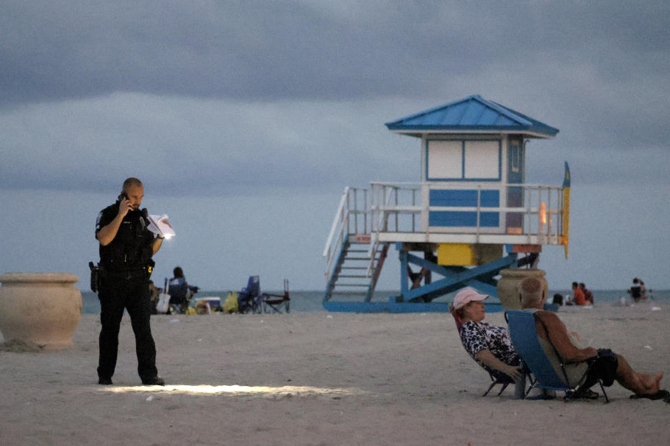 A police officer shines his flashlight downward as he pauses on Hollywood Beach while investigating a shooting Monday, May 29, 2023, in Hollywood, Fla. Multiple people were injured Monday evening when gunfire erupted along the beach boardwalk. (Mike Stocker/South Florida Sun-Sentinel via AP)