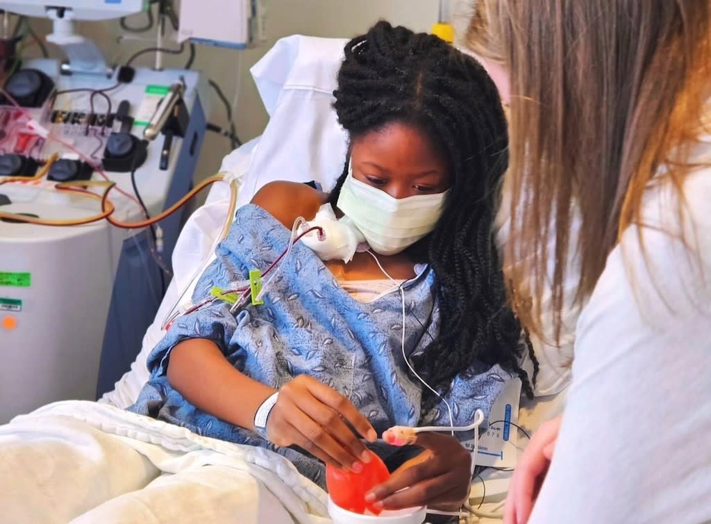 A young woman in a blue hospital gown in a hospital bed receiving a blood transfusion.