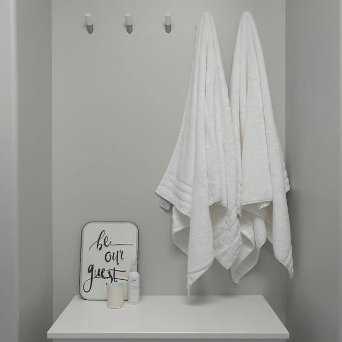 Two towels hung on hooks above a shelf with a 'be our guest' sign and toiletries