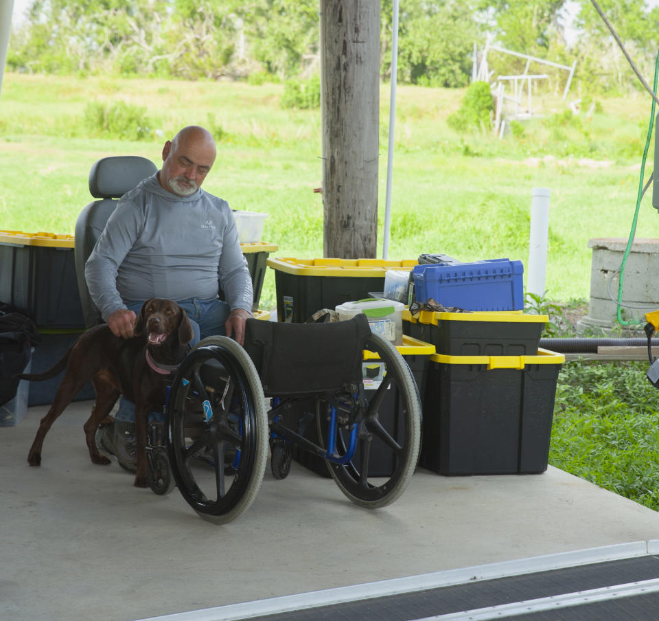A man in a wheelchair pets a dog.