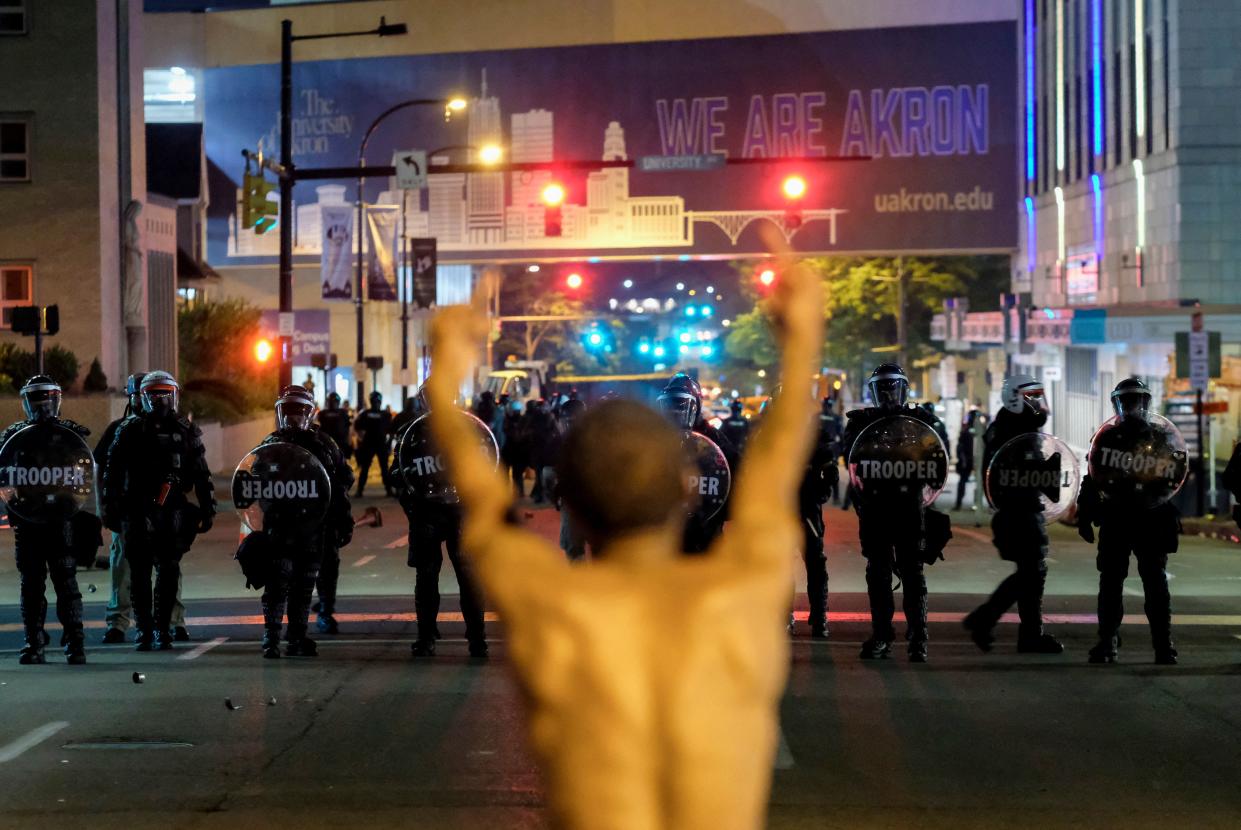 A shirtless man gestures toward troopers in riot gear during a protest.