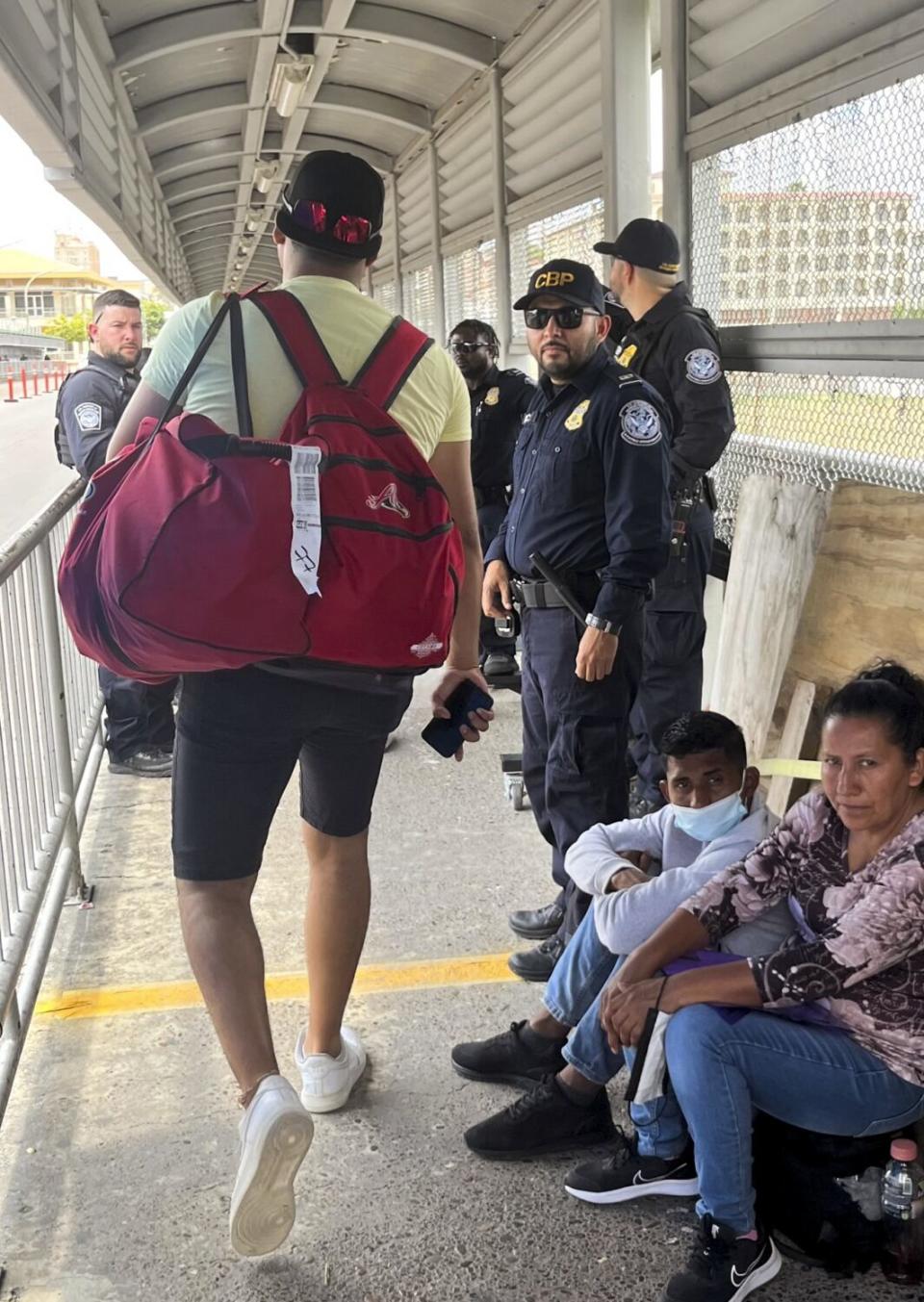 A Veracruz baseball player crosses the border, walking past people and by a yellow line on the pavement.