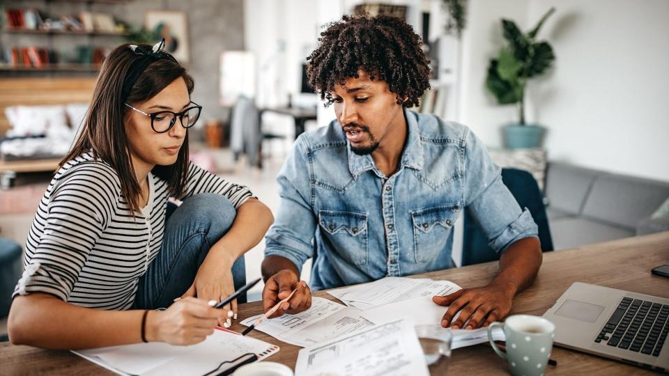 Modern married multi-ethnic young couple calculating financial bills at home.