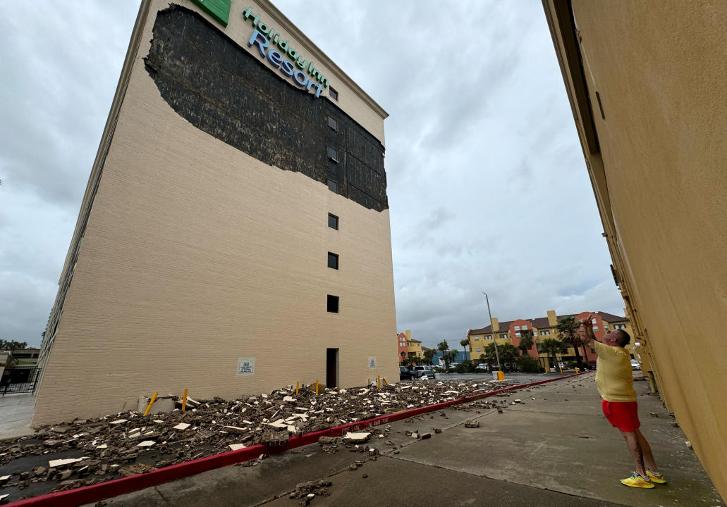 A man looks up and takes a picture of the damage at a Holiday Inn Resort. Debris can be seen scattered about at the base of the building.