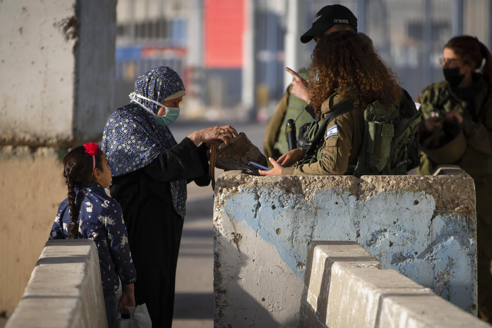 FILE - Israeli soldiers check a Palestinian women as she wait to cross the Qalandia checkpoint between the West Bank city of Ramallah and Jerusalem, Friday, April 23, 2021. The apparent comeback of former Prime Minister Benjamin Netanyahu and the dramatic rise of his far-right and ultra-Orthodox allies in Israel's general election this week have prompted little more than shrugs from many Palestinians. (AP Photo/Majdi Mohammed, File)