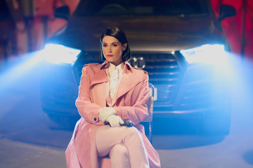 woman sitting on a chair outside at night with the headlights of a car behind her giving her light