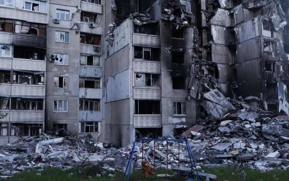 A teddy bear hangs on a swing next to a damaged building in Kharkiv  - RICARDO MORAES /REUTERS