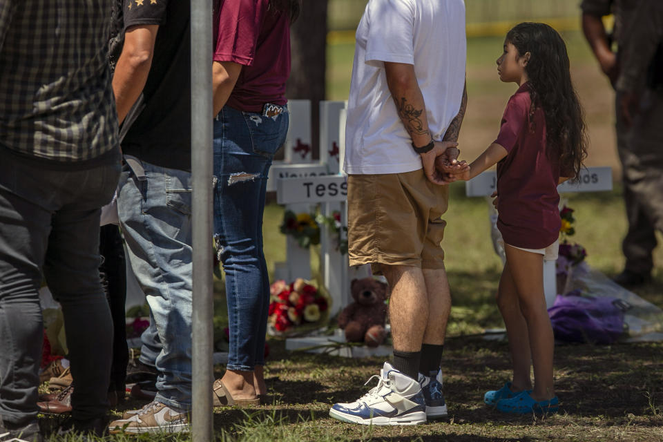 A young person holds onto an adults hand as they visit the memorial created outside Robb Elementary School in Uvalde, Texas, on Thursday, May 26, 2022. On Tuesday, a gunman entered the school and at least 19 students and two educators were killed./The San Antonio Express-News via AP)